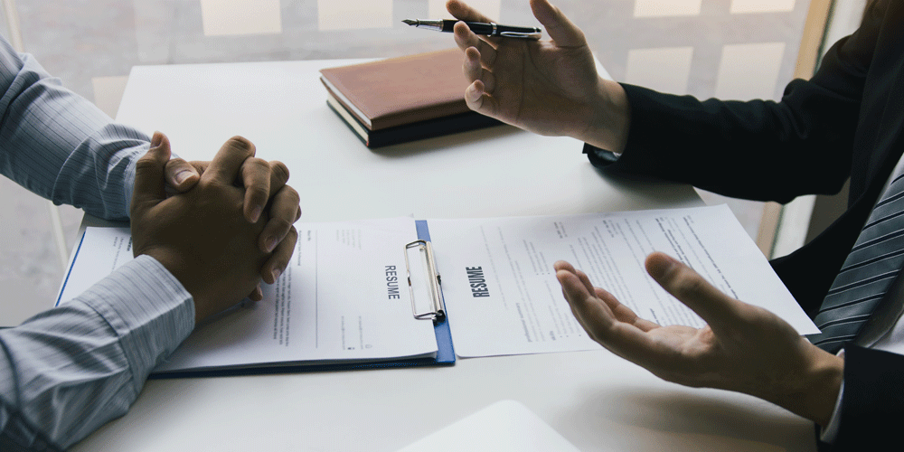 Job interview concept. Two people sit at a desk talking with their hands. Resumes are in front of them.